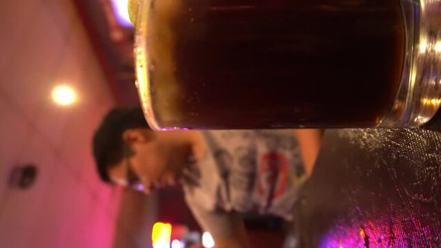 vertical close-up shot of cuba libre with the background of a man drinking beer in a bar