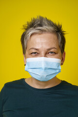 Happy eyes smiling grey short haired doctor woman wearing medical face mask looking at camera wearing green blouse isolated on yellow background