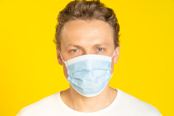 Handsome blond man wearing medical face mask prevention pandemic coronavirus or monkeypox. Handsome man in white t-shirt and medical mask on yellow background. Panoramic, healthcare concept