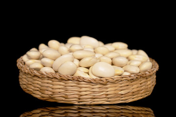 Uncooked white beans in a straw plate, close-up, isolated on a black background.