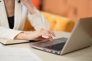 On face visible business woman in white jacket or suit at the desk working on laptop and making notes. Model female posing in business suit in the office. Business concept