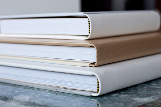 Macro photo of three closed photobooks in white and beige, lie on a glossy textured blue tabletop.