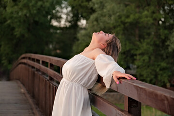 Fototapeta premium a beautiful girl in a white dress stands on a wooden bridge.