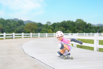 asian child or kid girl enjoy playing skateboard or surf skate in skatepark track to extreme sports exercise by crouching turn or person smile wearing helmet elbow knee support for body safety protect