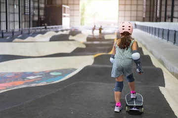 Poster back asian child or kid girl playing surf skate or skateboard and start on indoor pump track in skatepark by extreme sports to wearing helmet elbow pads wrist and knee support for body safety protect © kornnphoto