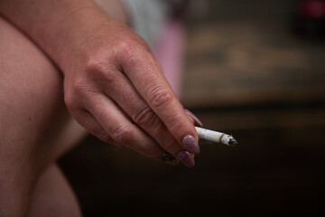 A woman's hand with an old manicure holds a cigarette