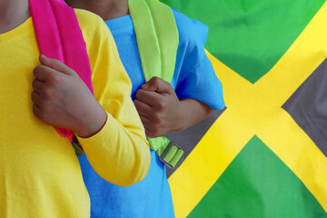 Two african children with satchels background of Jamaica flag. The concept of raising and educating children in Jamaica - obrazy, fototapety, plakaty