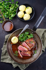 Traditional barbecue gourmet duck breast filet with skin served with potato dumplings in dark beer sauce as top view in a rustic skillet
