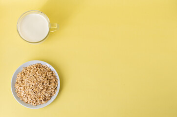 Flatlay white milk, oat flakes on a white plate on a yellow background, top view, the concept of healthy eating and preparing a healthy breakfast. Space for text on the right. Quality photo. High