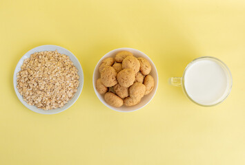 Flat lay white milk, oatmeal, and oatmeal cookies on a white plate on a yellow background, top view, the concept of healthy eating and preparing a healthy breakfast. Quality photo. High-quality photo