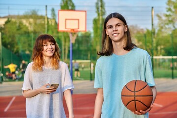 Portrait of young guy playing basketball on an outdoor game court, girl is out of focus.