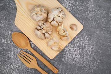 Fresh raw garlic on cutting board display with fork and spoon on dark background for cooking concept set up