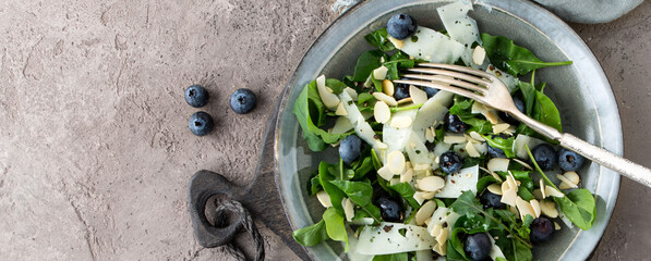 plate with salad with arugula, blueberries, cheese and almonds on a light table