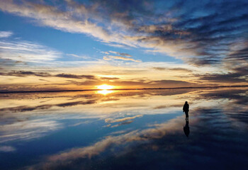 Fototapeta premium A person looking at the reflective sunrise at Uyuni Salt Flat, Bolivia