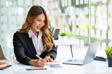 Asian businesswoman working on laptop and taking notes at the office