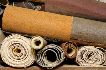 Multi-colored sandpaper in rolls lying on a shelf. Old emery paper in rolls