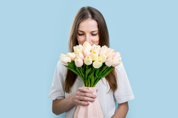 Young woman smelling fragrance while holding vase with bouquet of tulips on blue background