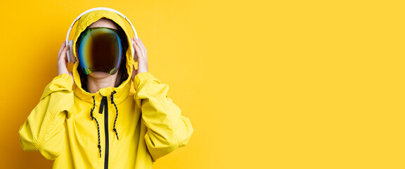 Young woman in cyberpunk glasses with headphones in a yellow jacket on a yellow background. Banner