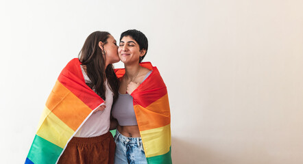 Lesbian couple wrapped in rainbow flag and giving a kiss