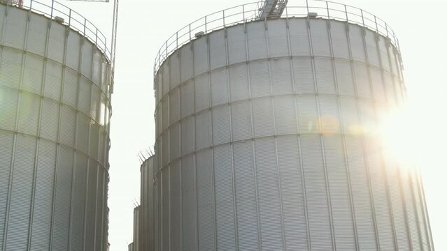 Silver silos on agro manufacturing plant for processing drying cleaning, storage of agricultural products, flour, cereals and grain. Large iron barrels of grain. Granary elevator.