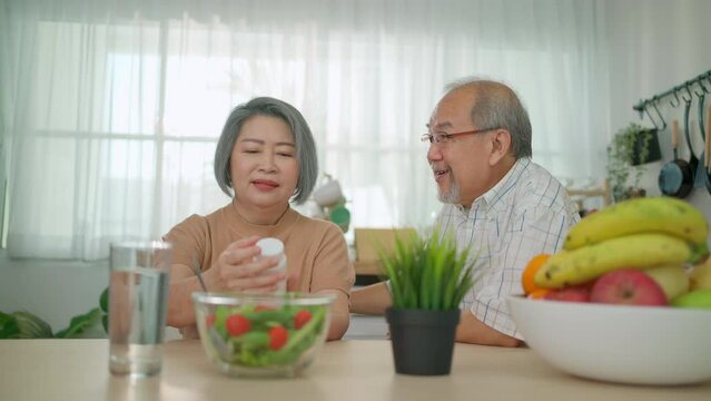 Elderly woman looking at vitamin or drug bottle and talk with senior mam sitting in the kitchen at home. Rehabilitation and healthcare concept. Asian senior with assisted living medication monitoring 