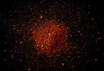 Spicy chili pepper flakes, crushed, milled dry paprika pile on black, top view