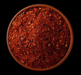 Spicy chili pepper flakes, crushed, milled dry paprika pile in clay pot isolated on black, top view