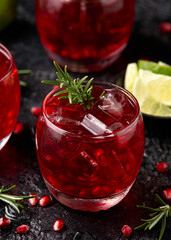 Pomegranate gin cocktail with lime, rosemary and ice on rustic black table