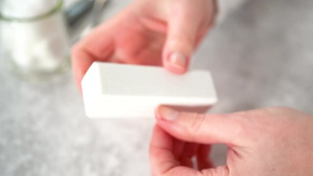 Woman finishing her manicure at home with simple manicure tools. Buffering nails with a nail buffer block.