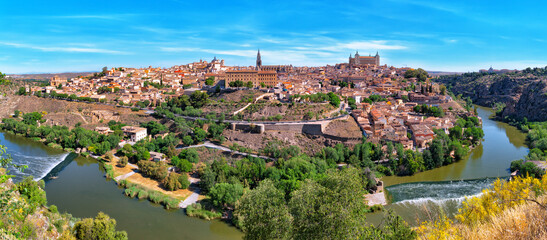 Naklejka premium Picturesque panorama of the ancient city of Toledo on the banks of the Tagus River on a sunny afternoon against the blue sky. Capital of the province of Toledo, community of Castilla–La Mancha, Spain