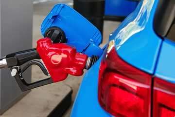 Blue car refueling on a petrol station, nozzle close-up