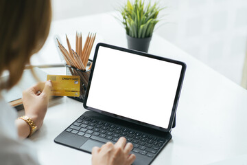 Mockup image of a woman holding credit card while using laptop with blank white screen in office.