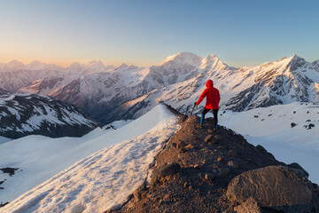 Naklejka na ściany i meble Snow-covered peaks at sunrise with lonely man on dark edge of mountain, Caucasus, Russia