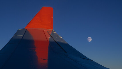 Full moon on a dark sky under the wing of an airplane with a red winglet