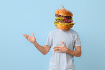 Man with tasty burger instead of his head showing something on light blue background