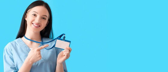 Female medical assistant pointing at her badge on light blue background with space for text