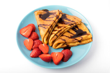 Delicious thin pancakes with strawberries and chocolate on a blue plate. White background