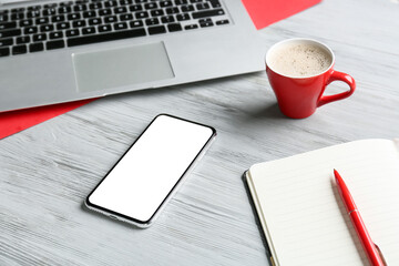 Mobile phone, cup of coffee, laptop and notebook on light wooden background