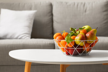 Basket with fruits on table near sofa