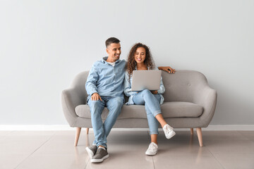 Young couple with laptop sitting on sofa near light wall