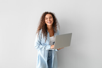 Happy young African-American woman using laptop on light background - obrazy, fototapety, plakaty