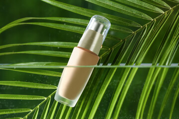 Tropical leaf and bottle of makeup foundation in water on green background