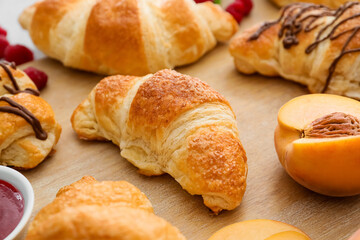 Wooden board of delicious croissants with peach on table, closeup