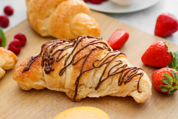 Wooden board of delicious croissants with chocolate and strawberry on table, closeup