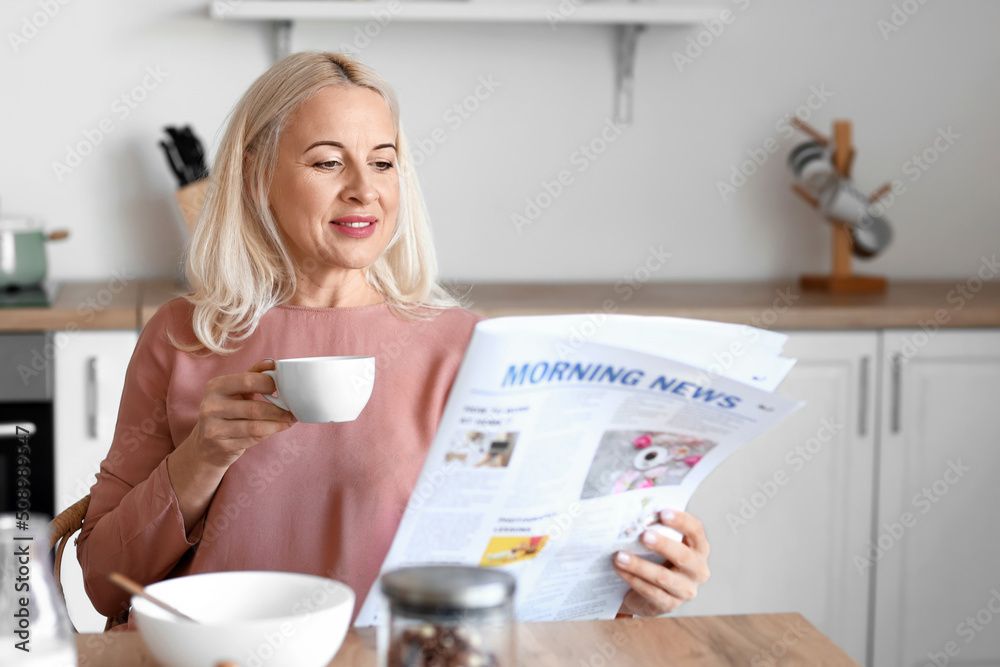 Wall mural Morning of mature woman drinking coffee and reading newspaper in kitchen