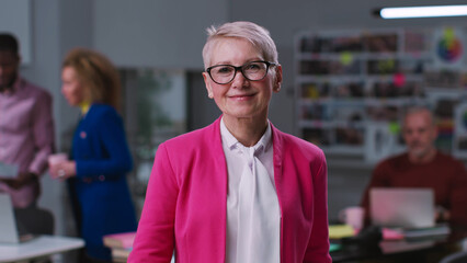 Portrait of stylish senior businesswoman smiling at camera standing in creative office