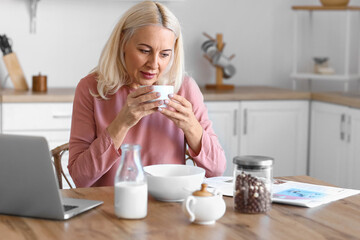 Morning of mature woman drinking coffee and reading newspaper in kitchen