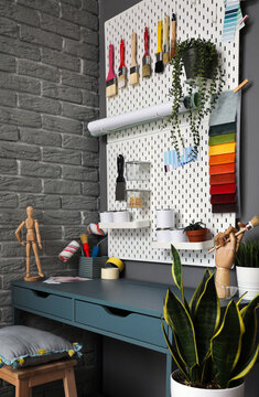 Pegboard with modern decorating tools and desk near grey brick wall