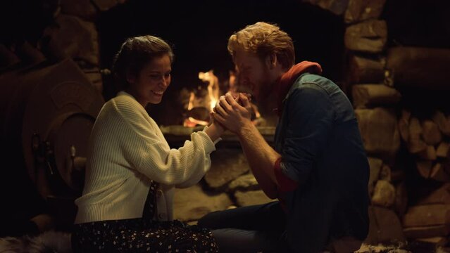 Loving couple warming fireplace in country house. Boyfriend girlfriend kiss hand