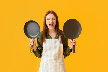 Angry young woman with frying pans on yellow background